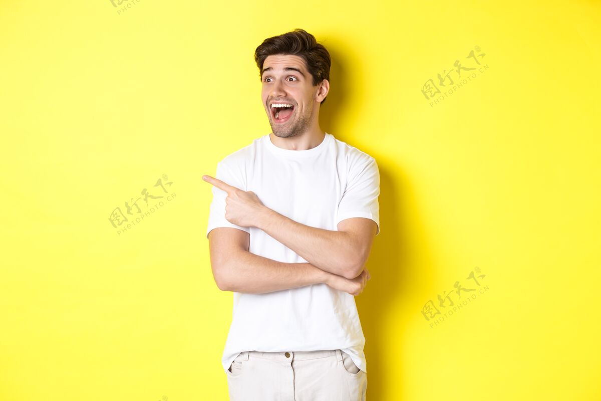 站兴奋的微笑着的男人指着左边 看着促销优惠 站在黄色的背景上工作室男人指