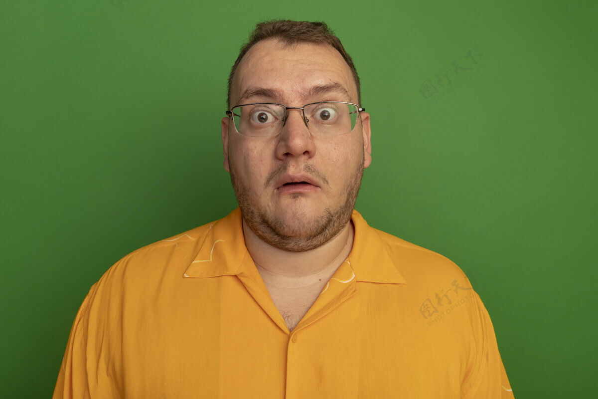 惊讶一个戴着眼镜 穿着橙色衬衫的男人站在绿色的墙上 既惊讶又担心担心看站着