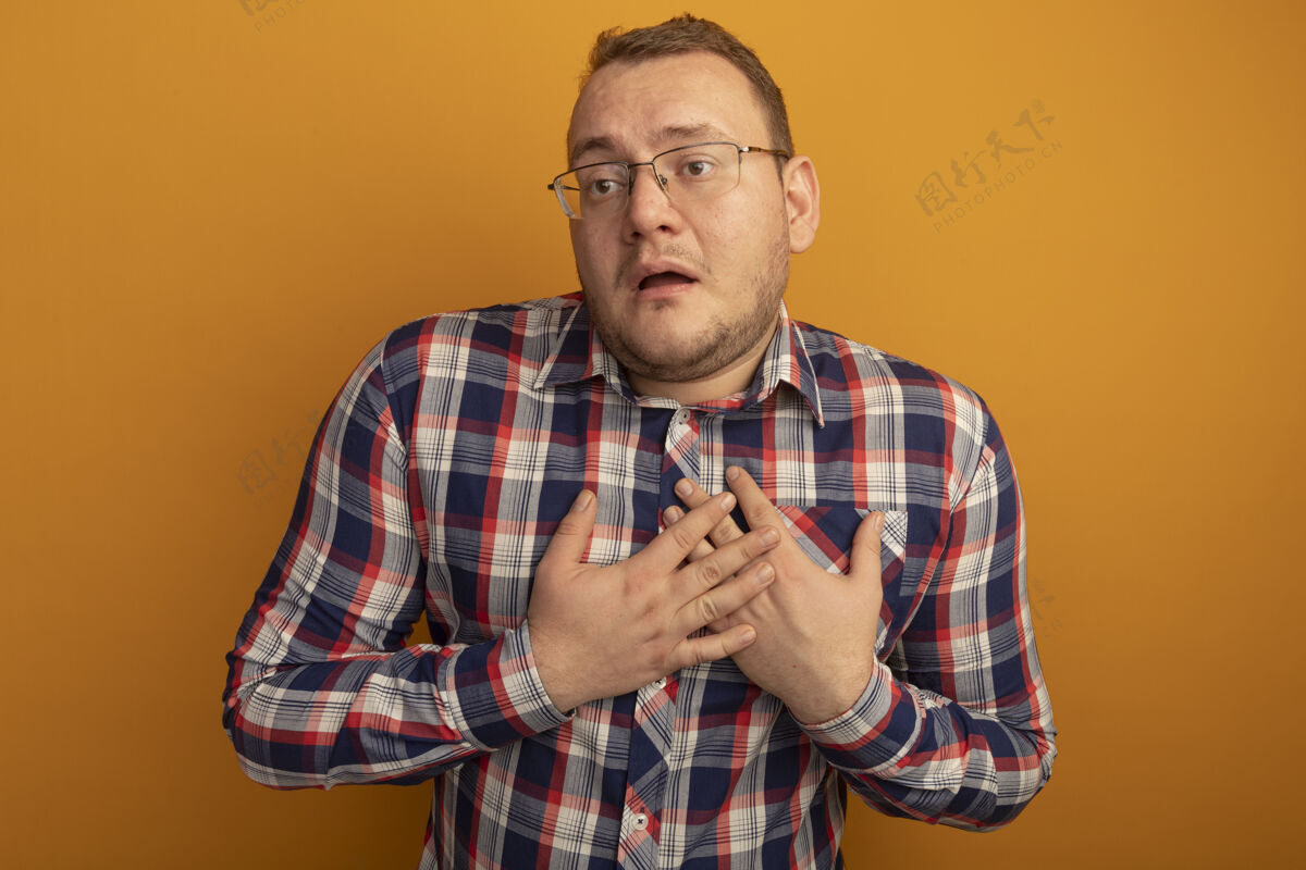 站着一个戴眼镜 穿着格子衬衫的男人站在橘色的墙上 双手放在胸前 焦急地看着一边胸膛手眼镜