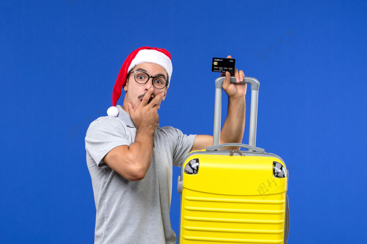 前面正面图年轻男子手持黄包银行卡上蓝墙旅游情感度假圣诞节工程师包