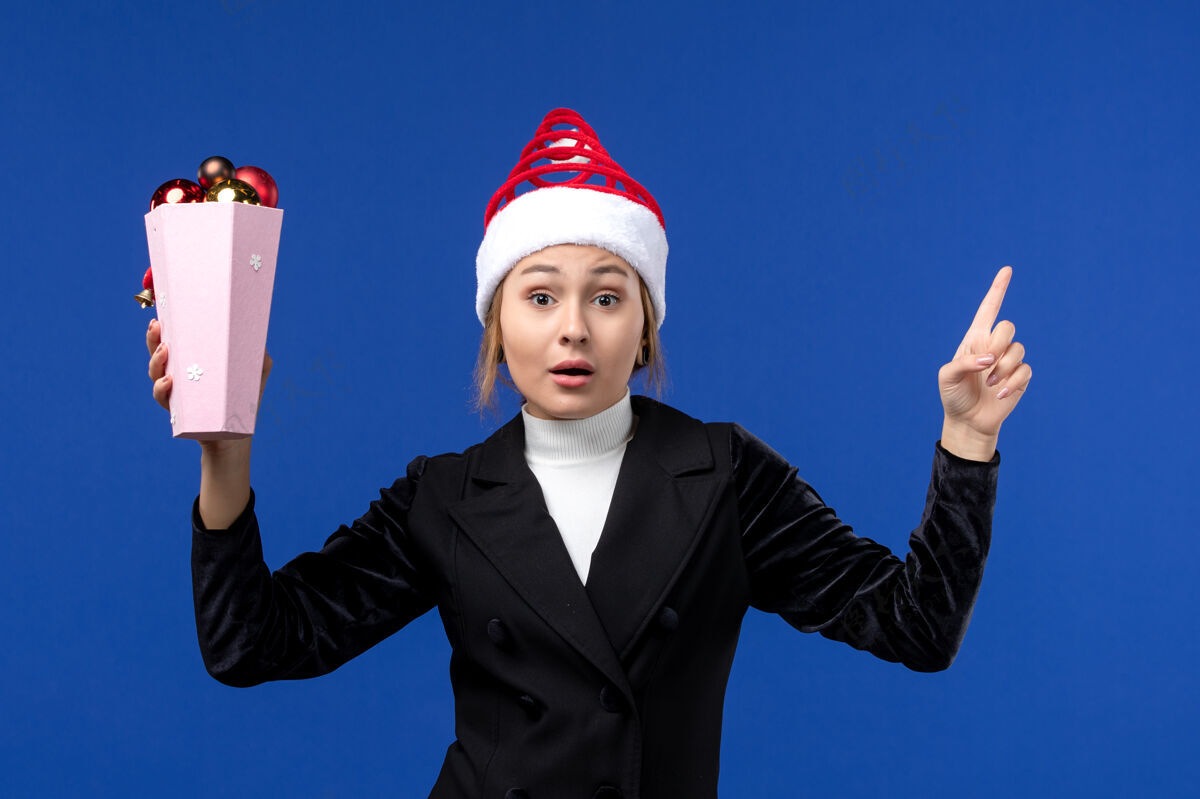 年轻女性前视图年轻女性拿着蓝色背景的圣诞树玩具新年妇女的颜色成功执行女人