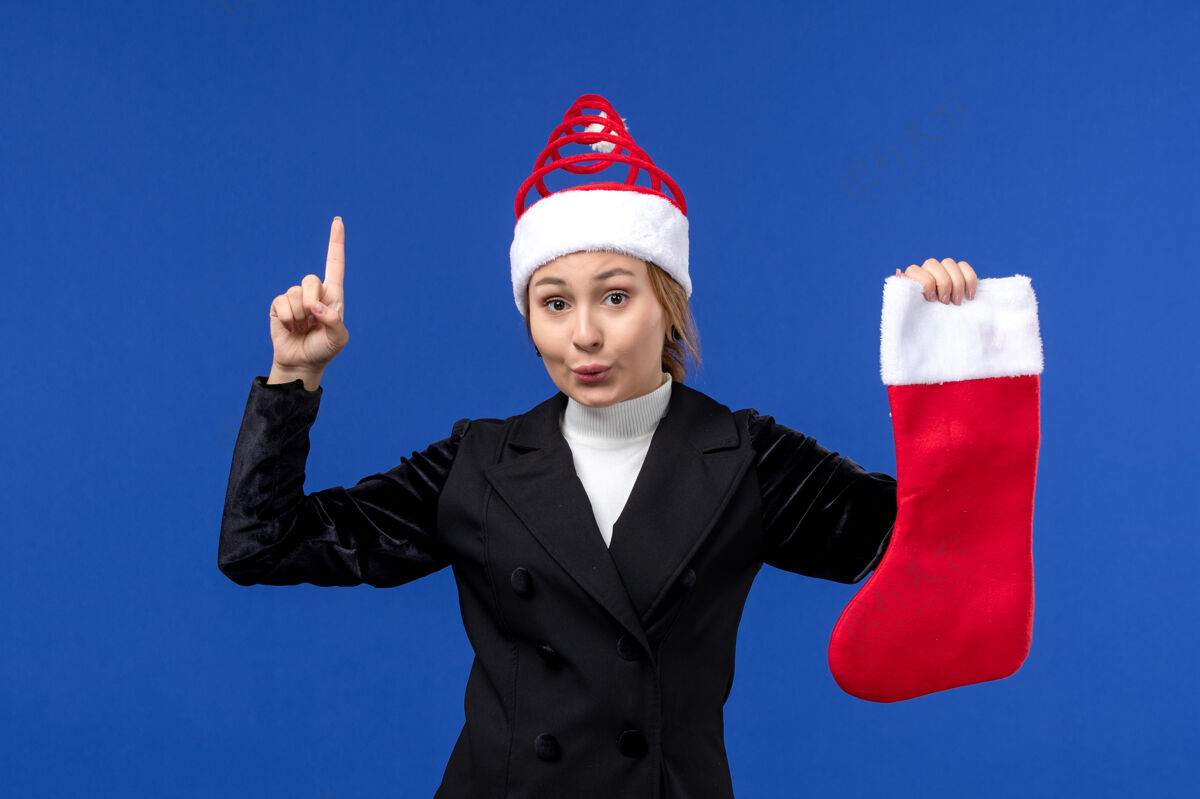 西装正面图：年轻女性手持红色圣诞袜在蓝色墙壁上度过人类的新年假期持有人工作