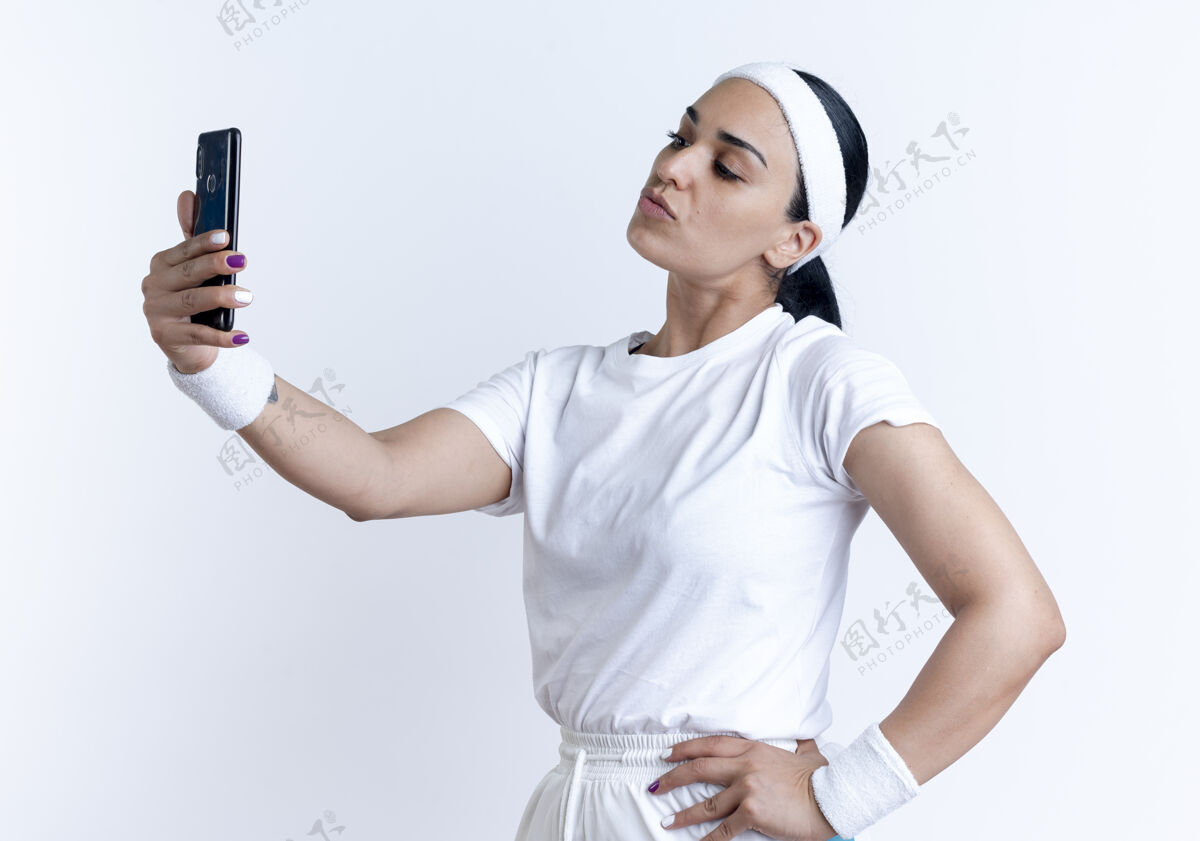 穿年轻自信的白人运动女性戴着头带和腕带站在一边看手机自拍隔离在白色空间与复制空间复制电话女人