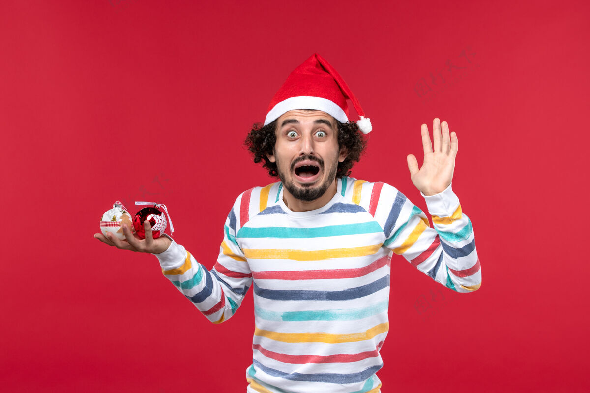 娱乐正面图年轻人拿着圣诞树玩具站在红墙上新年红人过节人人人