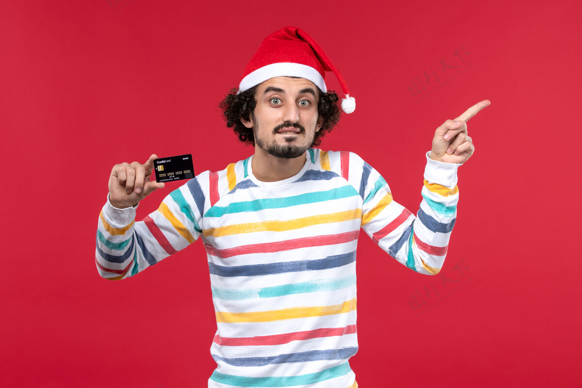 圣诞节正面图年轻男子手持黑色银行卡红墙钱红年过节成人娱乐微笑