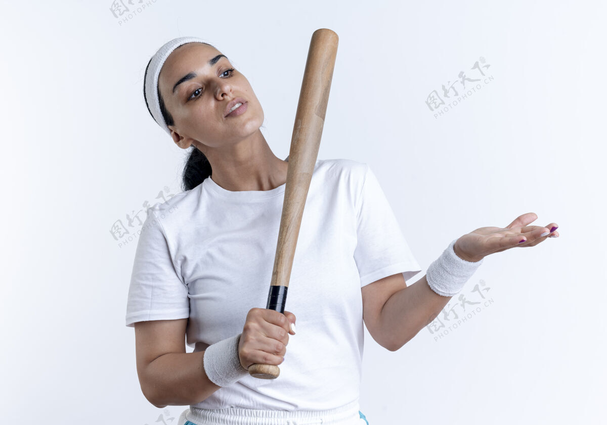 女人年轻自信的白人运动女性戴着头带和腕带拿着球棒看着并指着隔离在空白处的一边蝙蝠腕带空间
