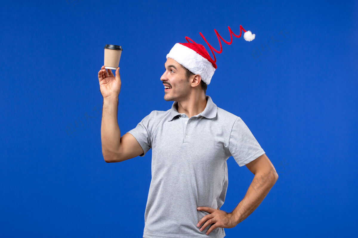 人正面图年轻男性手持塑料咖啡杯在蓝色墙壁上过年男性节日男前面抱