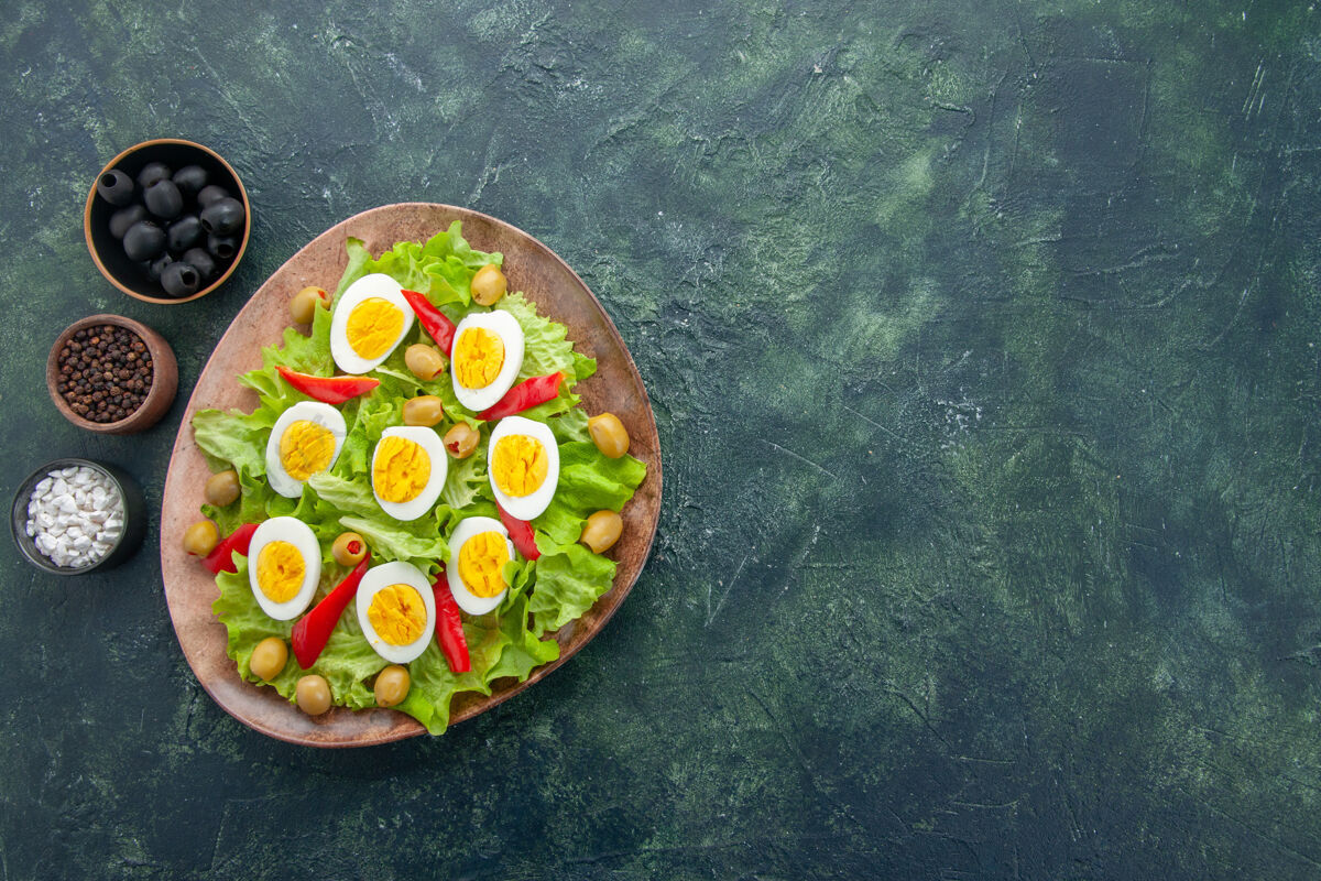 深色俯视图美味的鸡蛋沙拉与绿色沙拉橄榄和调味品在深蓝色的背景顶部煮鸡蛋绿色