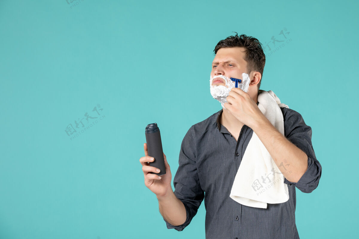 头发正面图：年轻男性在蓝色背景上用剃刀刮脸年轻男性肖像洗澡