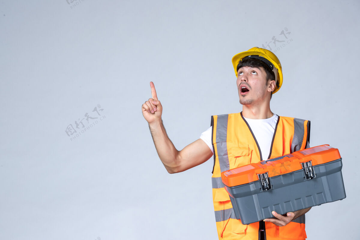 工具正面图：年轻的男工人拿着沉重的工具箱 背景是白色的建设者人视图