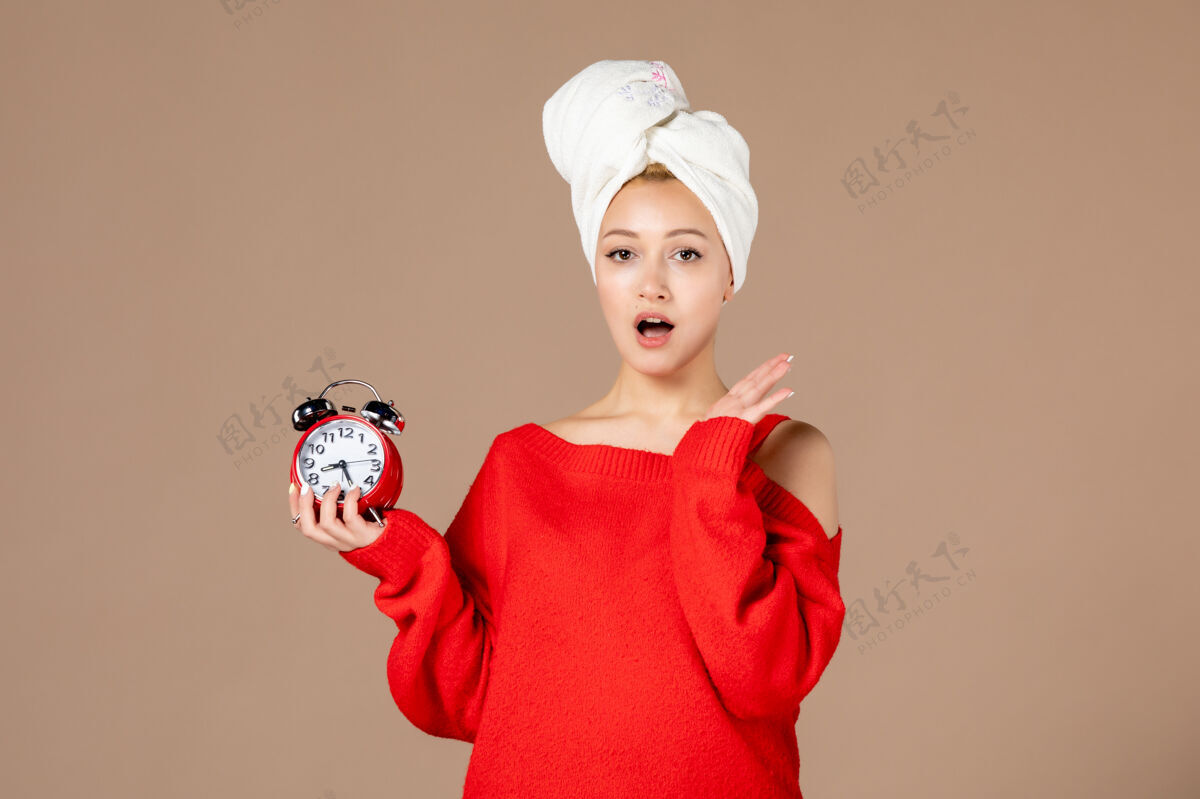 肖像正面图：年轻女性 头上戴着时钟和毛巾 背景为粉色前面风景面霜