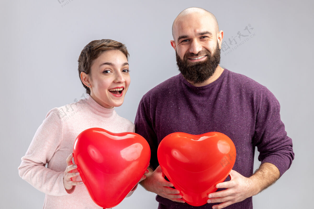 形状一对穿着休闲服的年轻夫妇手持心形气球 站在白色背景上 看着相机 开心又惊喜地庆祝情人节年轻庆祝看