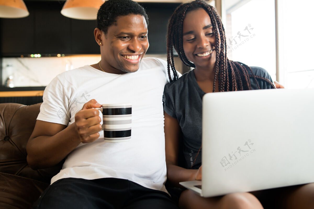 房子一对年轻夫妇坐在家里的沙发上 一起度过时光 使用笔记本电脑的照片新的正常生活方式理念沙发坐放松