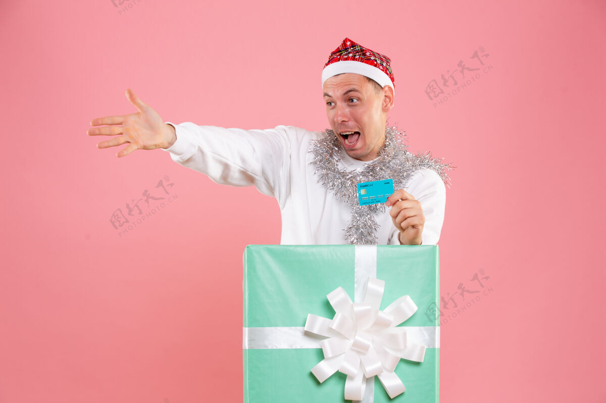 银行正面图里面的年轻男性手持粉色背景的银行卡粉色圣诞节礼物