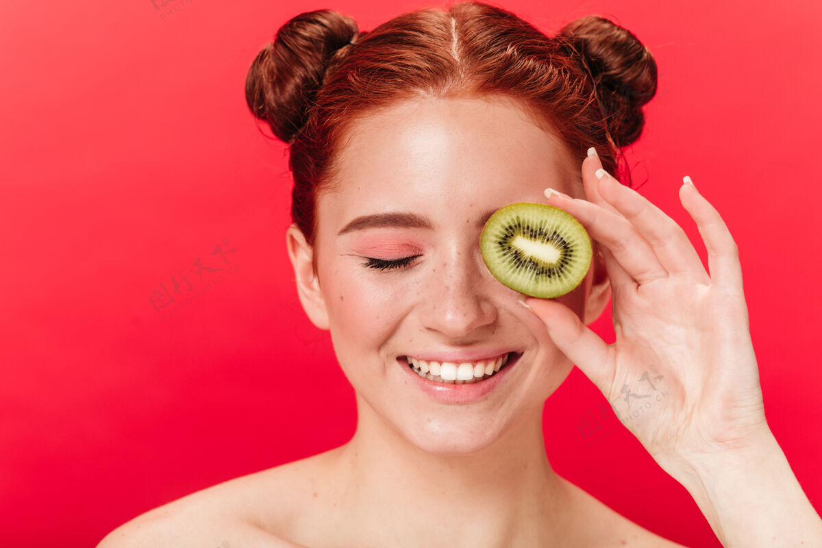 孤立的红色带着奇异果的欢笑女人的正面图带着奇异水果的兴奋的姜女孩的摄影棚镜头女士红发猕猴桃