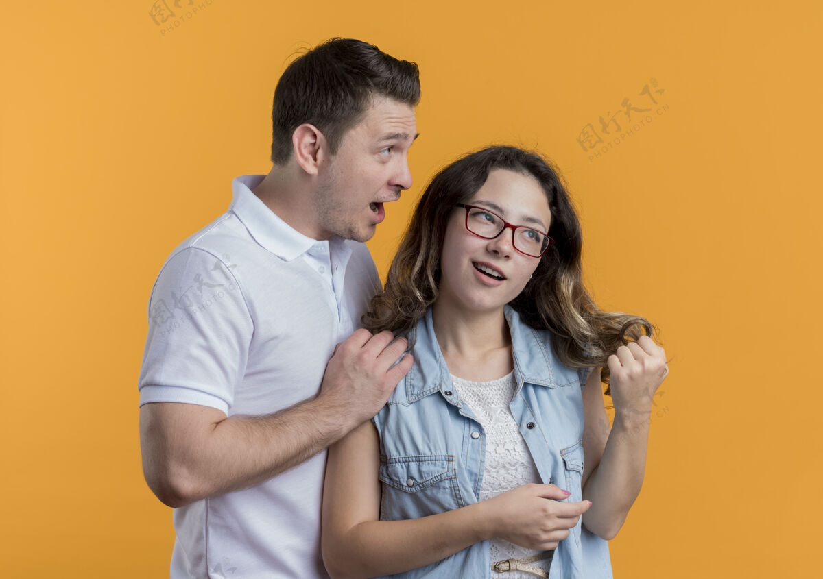 男人一对年轻夫妇穿着休闲服的男人和他的女朋友聊天 看着橙色的惊讶女人情侣橙色