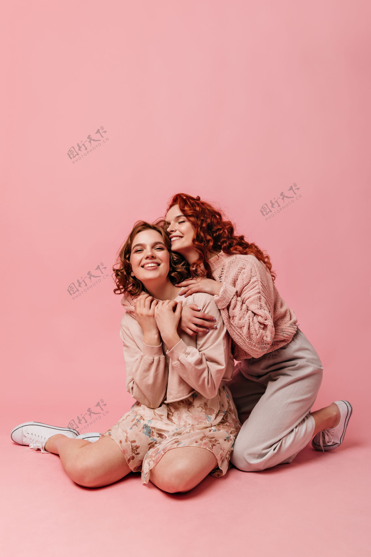 友谊情绪化的漂亮女孩坐在粉色背景上两个朋友在地板上合影拥抱快乐粉色女性
