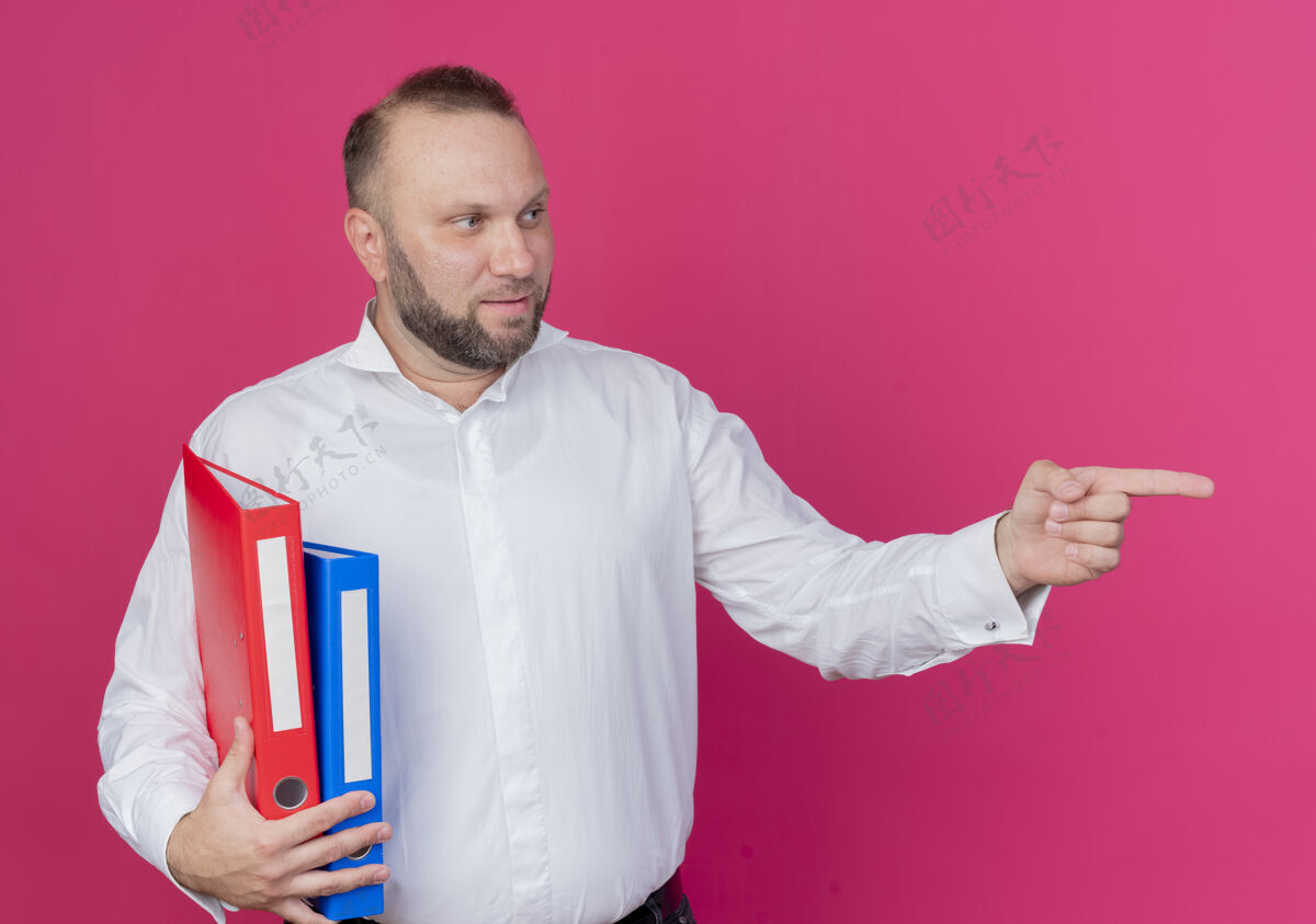 东西一个留着胡子的男人穿着白衬衫 拿着文件夹 用食指指着粉色的东西看向一边男人穿手指