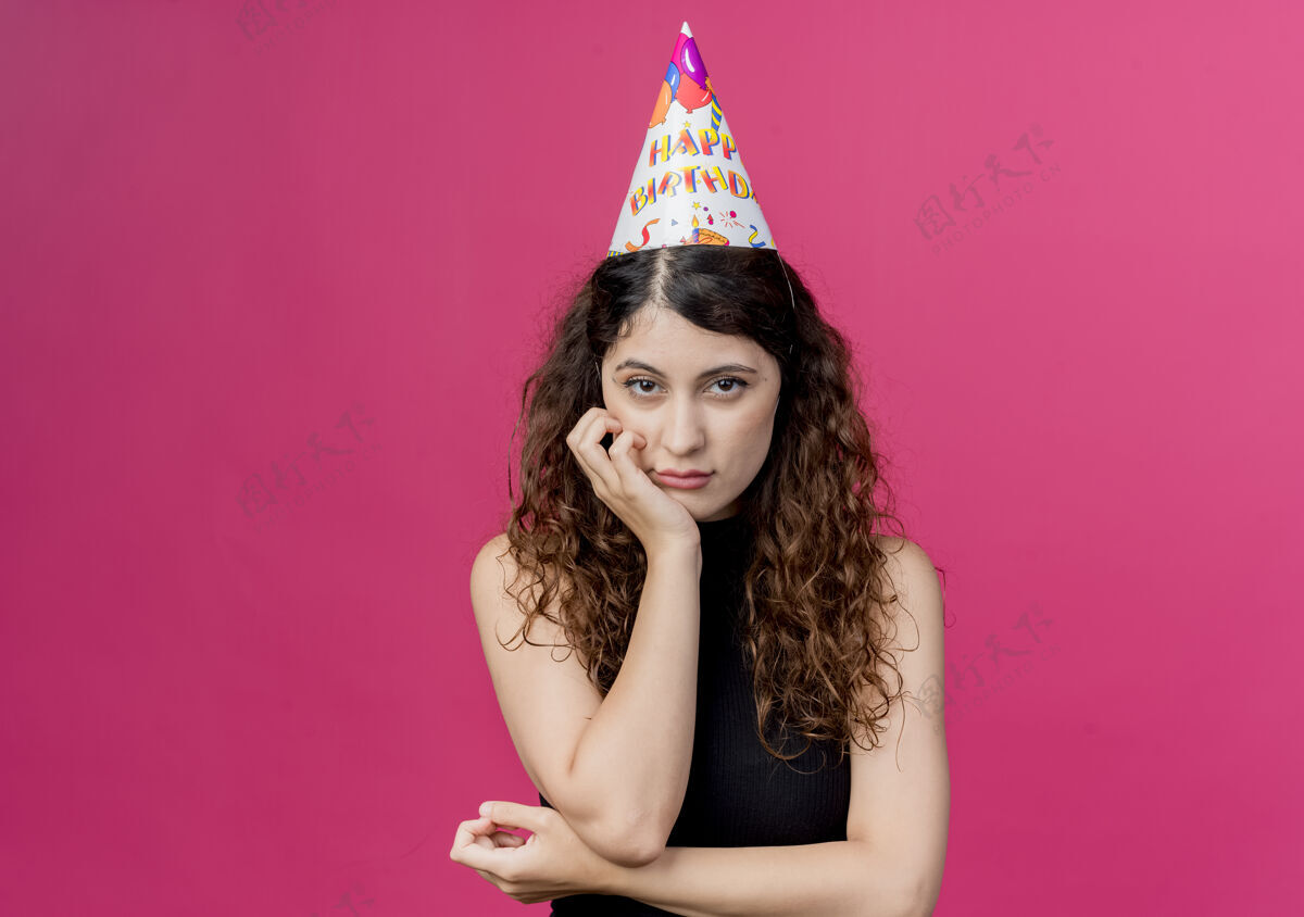 生日年轻漂亮的女人 卷发 戴着节日帽 悲伤的表情 生日派对概念 粉色节日卷曲年轻