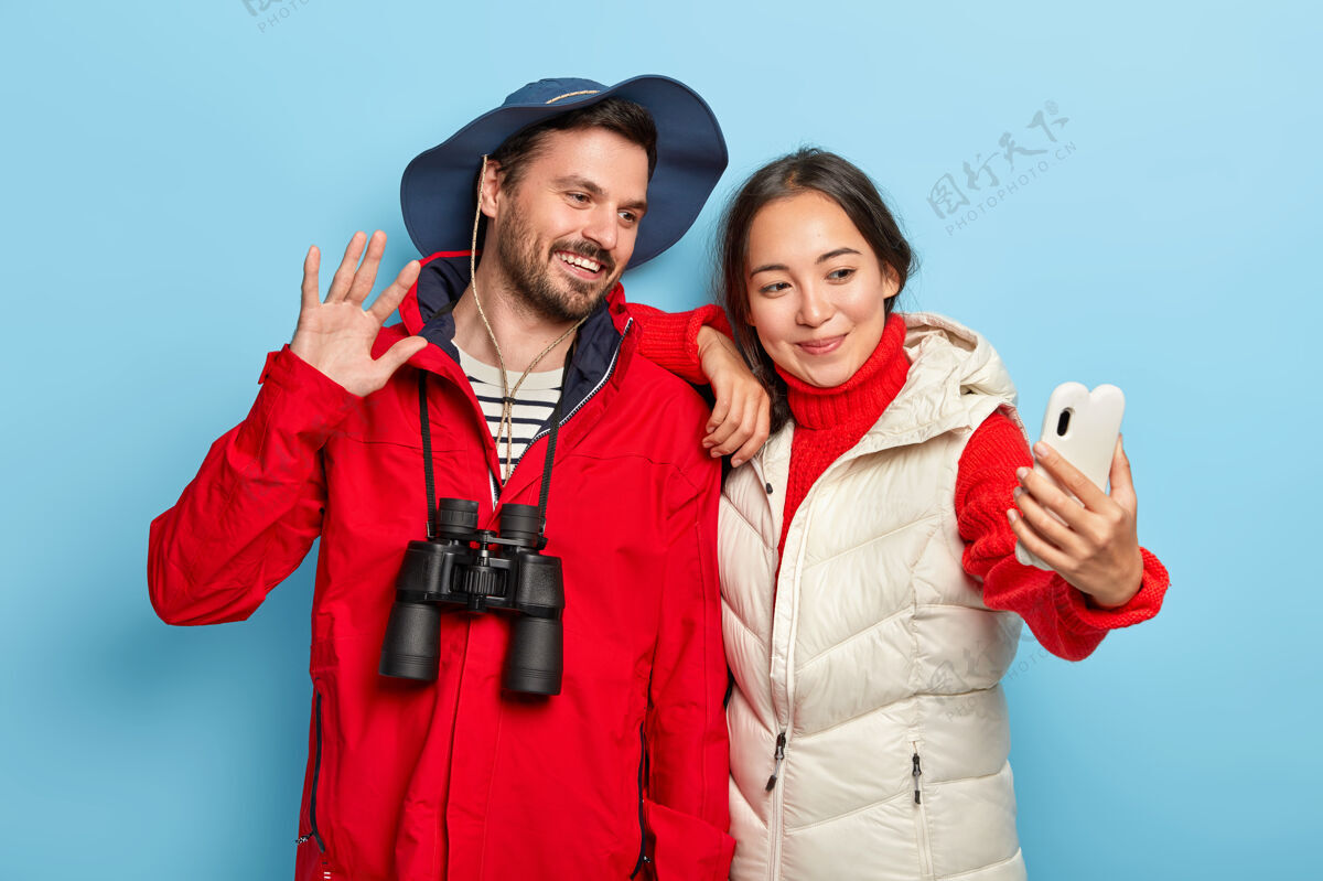 设备快乐的混血情侣在智能手机上自拍 享受徒步旅行 站得很近 穿着休闲服 用望远镜远足关系穿着