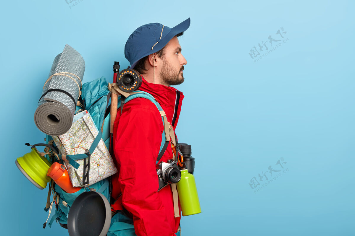 旅游严肃的男性背包客带着大背包站着 带着许多旅行和休息的必需品 独自去露营 探索新的环境 穿着红色夹克和帽子休闲胡子严肃