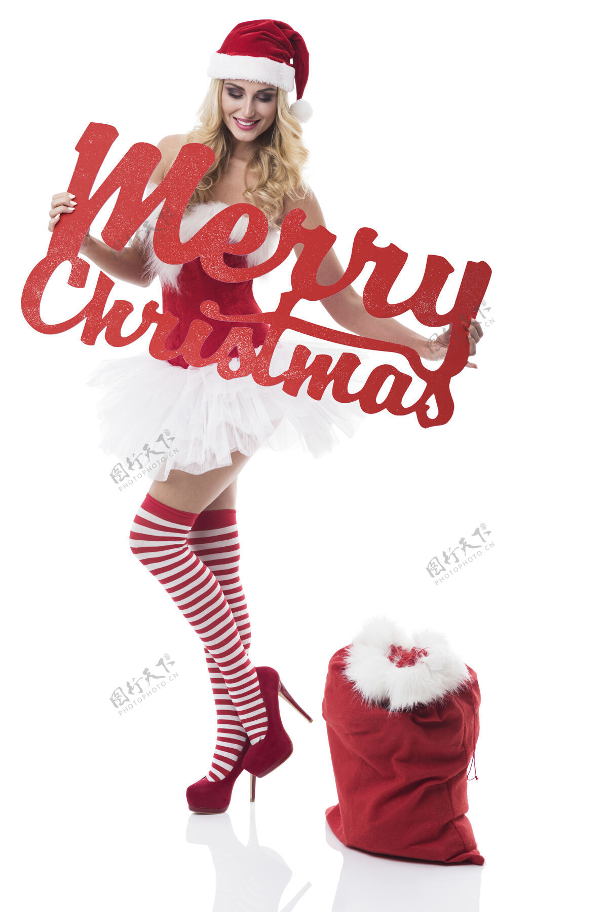 连衣裙穿着圣诞老人服装的性感女人在白墙上摆姿势皮草微笑圣诞快乐