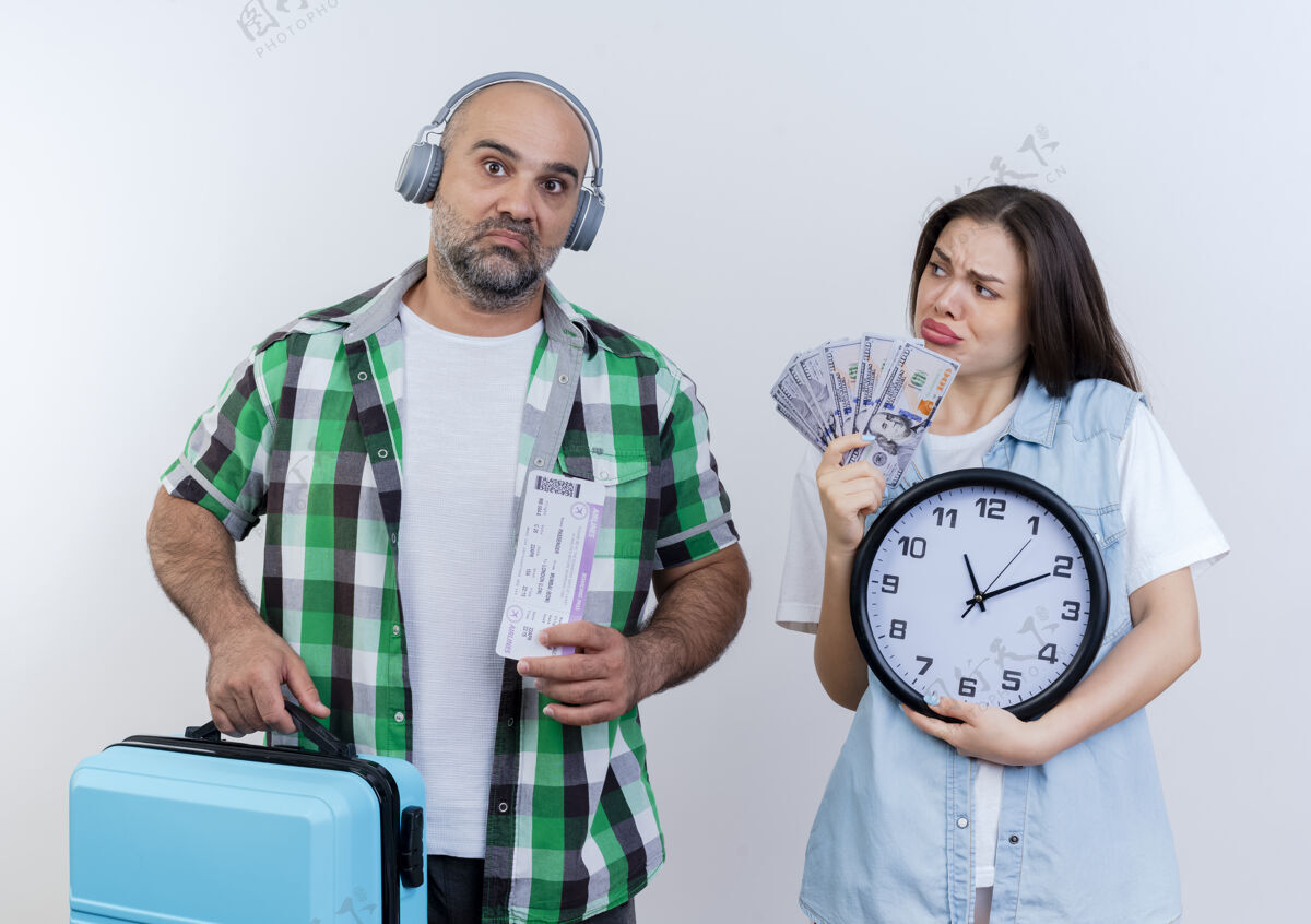 看悲伤的成年旅行者夫妇戴着耳机拿着旅行票和手提箱的男人拿着钱和时钟看着他穿男人耳机