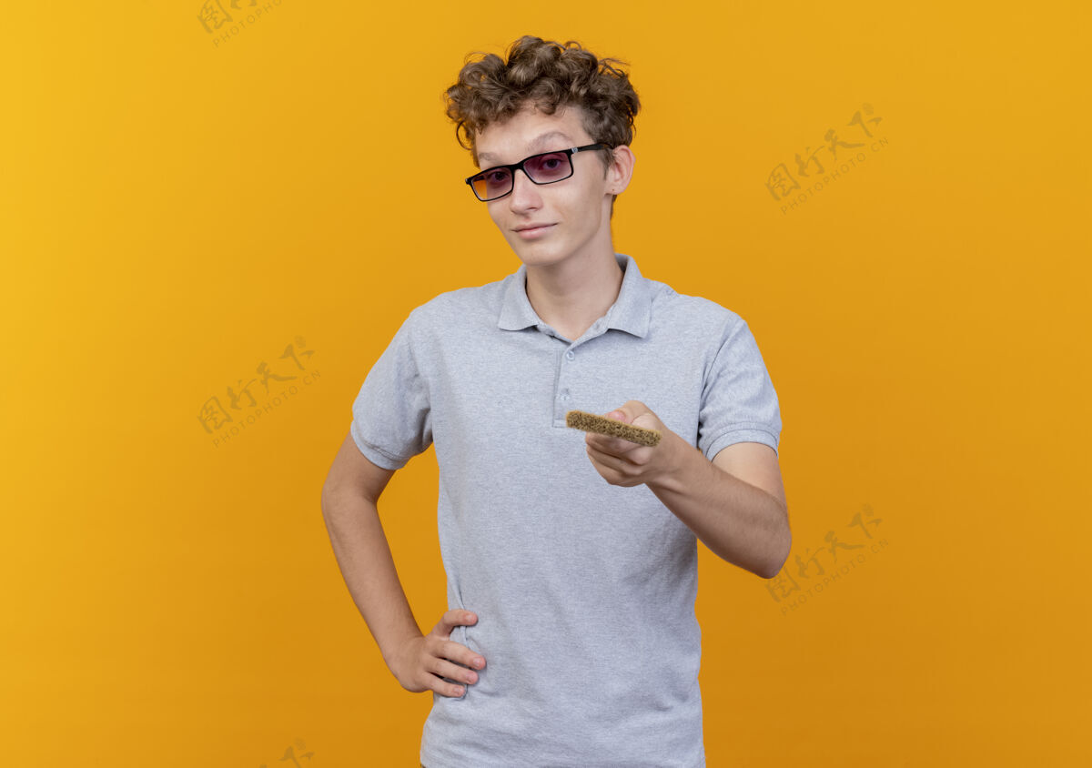 男人一个戴着黑眼镜的年轻人穿着灰色马球衫 手里拿着画笔 在橙色上方对着镜头献礼穿站着提议