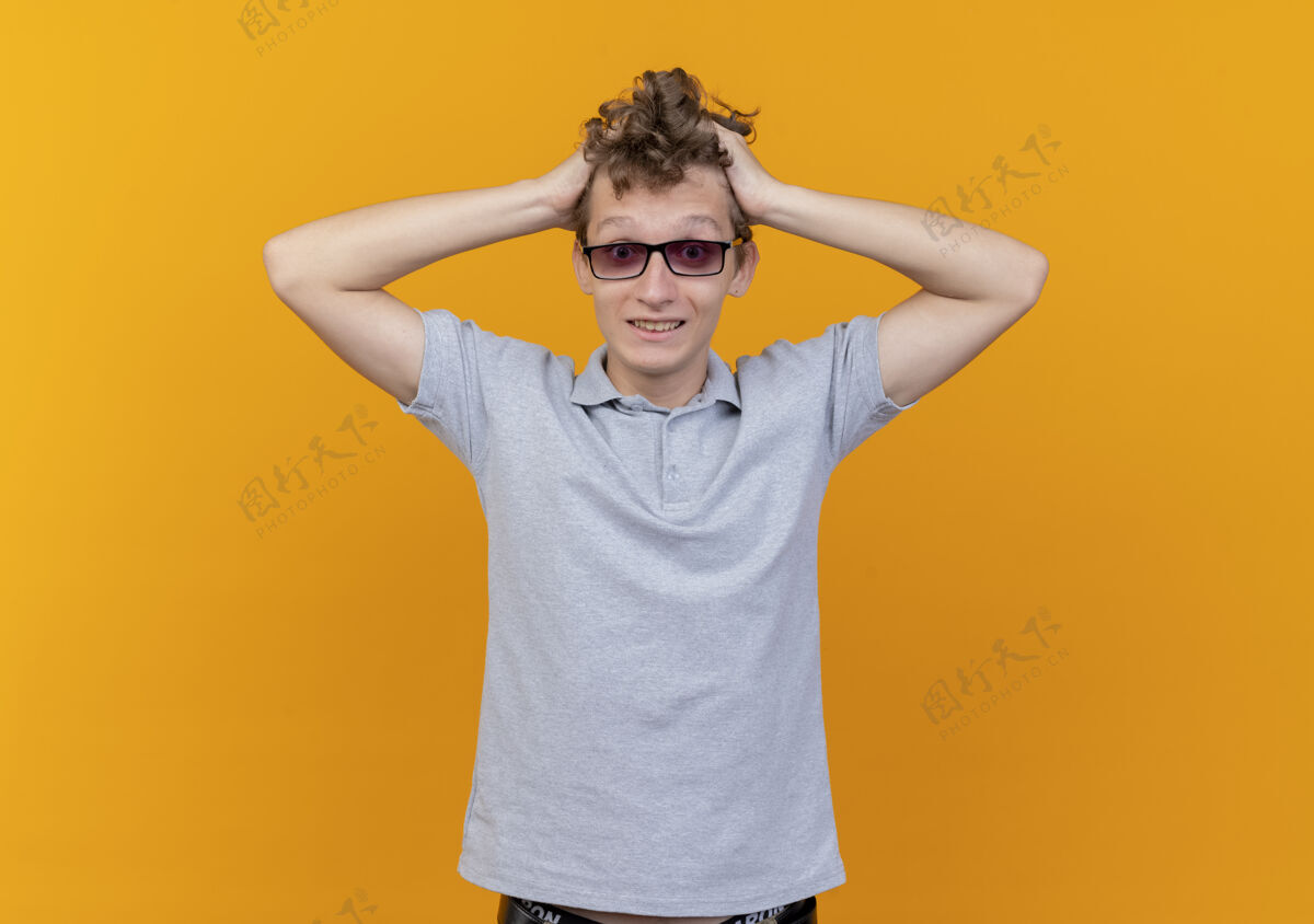 站着一个戴着黑眼镜 穿着灰色马球衫的失望的年轻人摸着他的头 被橙色弄糊涂了男人头衬衫