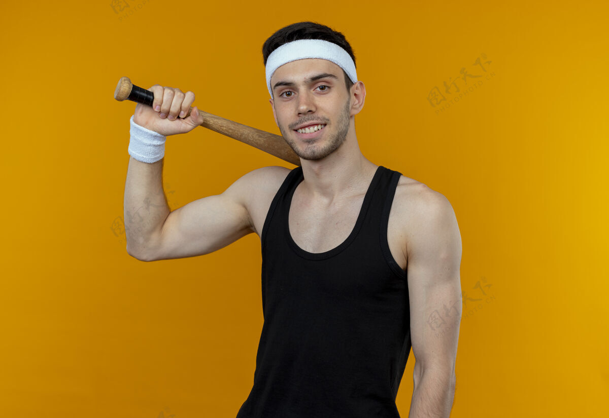 微笑年轻的运动型男子戴着棒球帽 站在橙色的墙上自信地微笑着头带站着运动