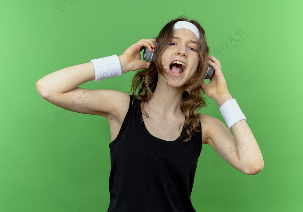 疯狂穿着黑色运动服 头戴耳机的年轻健身女孩疯狂地享受着她最喜爱的音乐头带绿色黑色