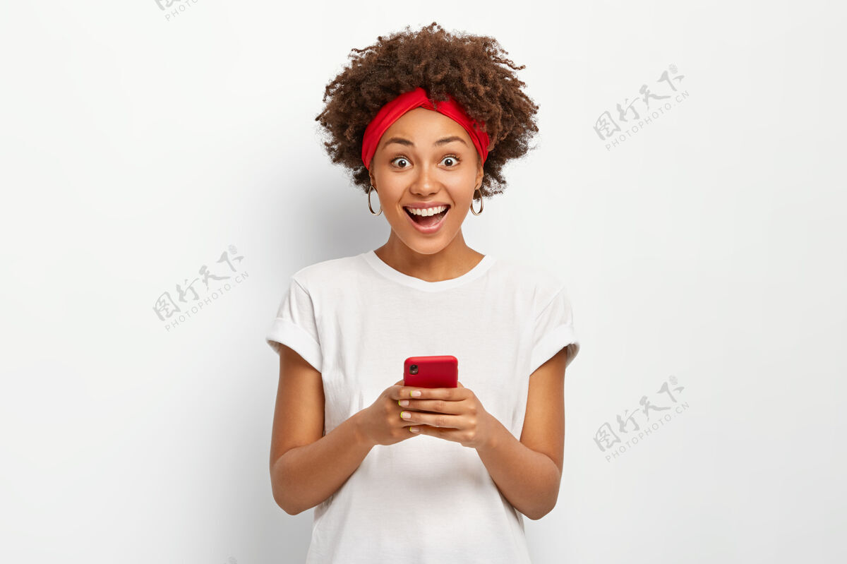 快乐微笑快乐的年轻女子手持现代手机 积极微笑 上网 创建自己的博客 穿着白色t恤休闲短信社交