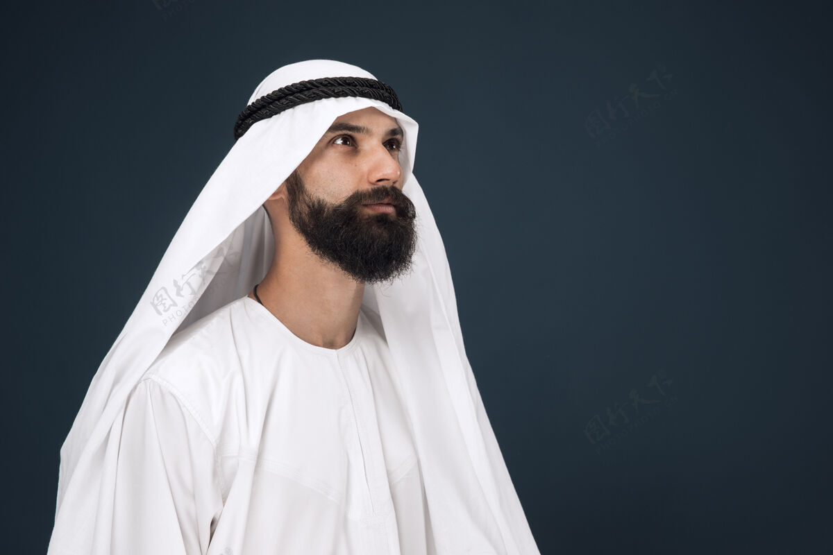 严肃深蓝色墙上的阿拉伯沙特商人半身像年轻的男模站着 看上去很体贴商业 金融 面部表情 人类情感的概念围巾情绪男性