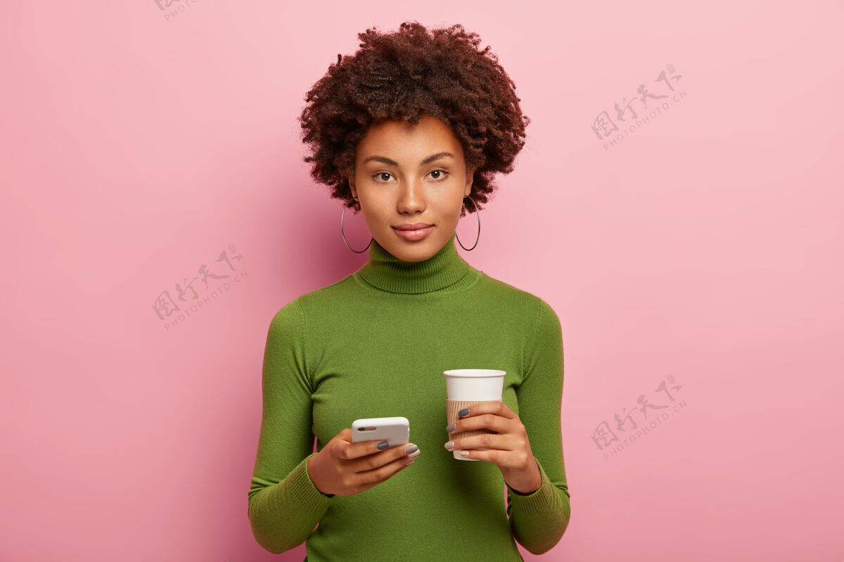 年轻漂亮女人端庄地看着相机 表情自信 拿着手机 在社交网络上看照片 喝外卖咖啡耳环网络交流