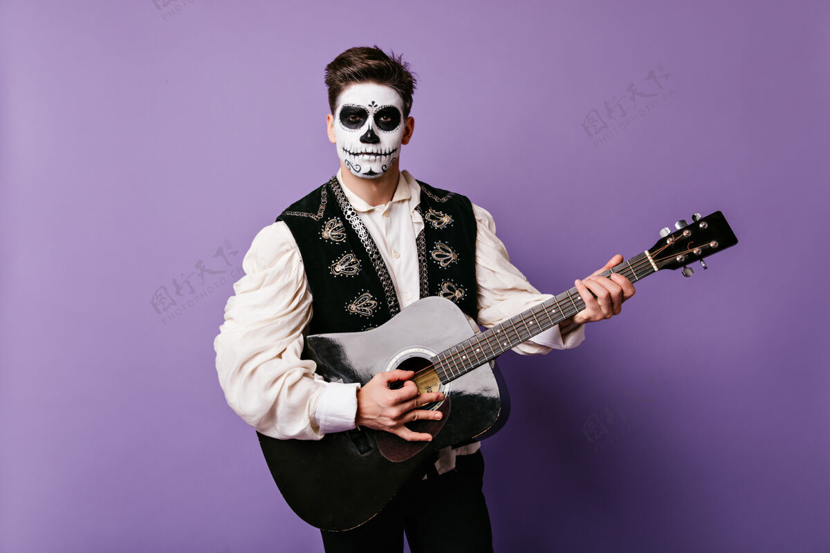 骷髅墨西哥嘉年华装扮的帅哥在弹吉他隔离墙上的深色特写肖像死亡死亡之日多彩