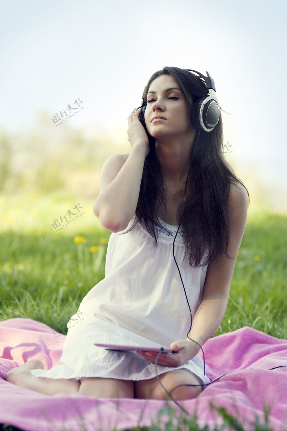 手持式在草地上听音乐的年轻女子笔记本白色毯子