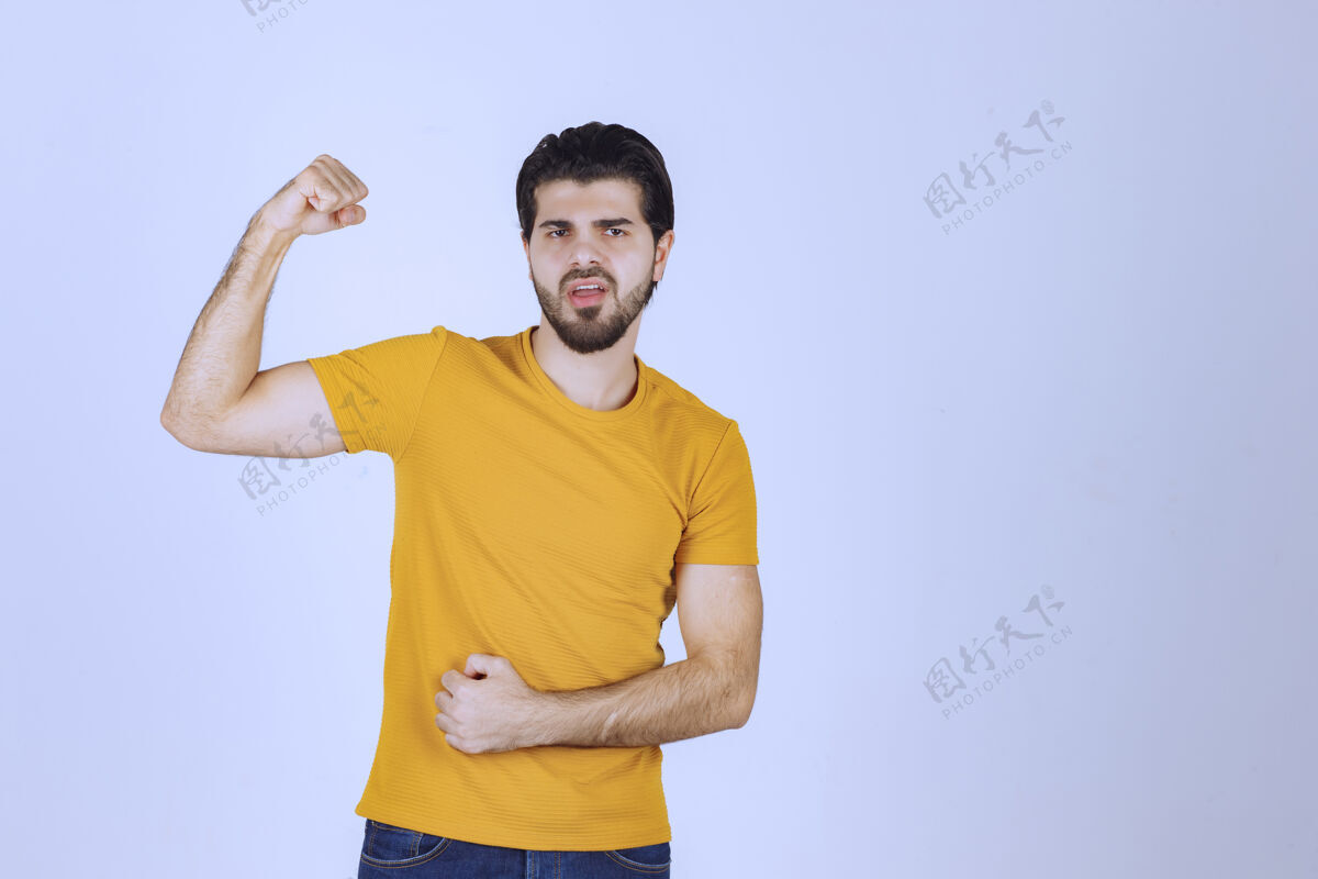 姿势穿黄衬衫的男人展示他的拳头和力量肌肉年轻聪明