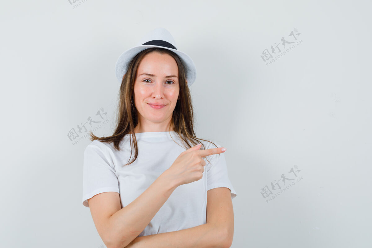 孩子年轻女孩穿着白色t恤 帽子指向一边 看起来很高兴 正面视图旁边指向肖像