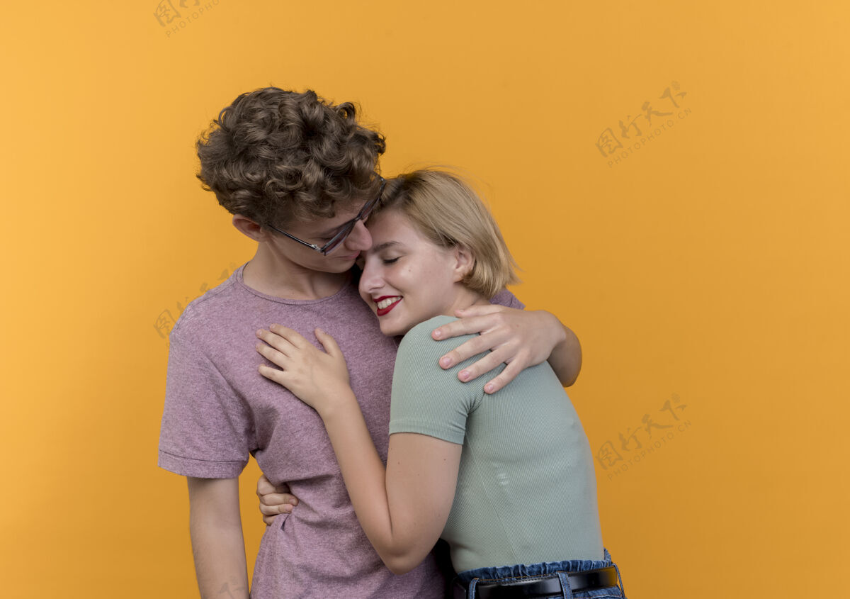 女人年轻美丽的夫妇站在一起幸福相爱拥抱站在橙色的墙上男人拥抱年轻