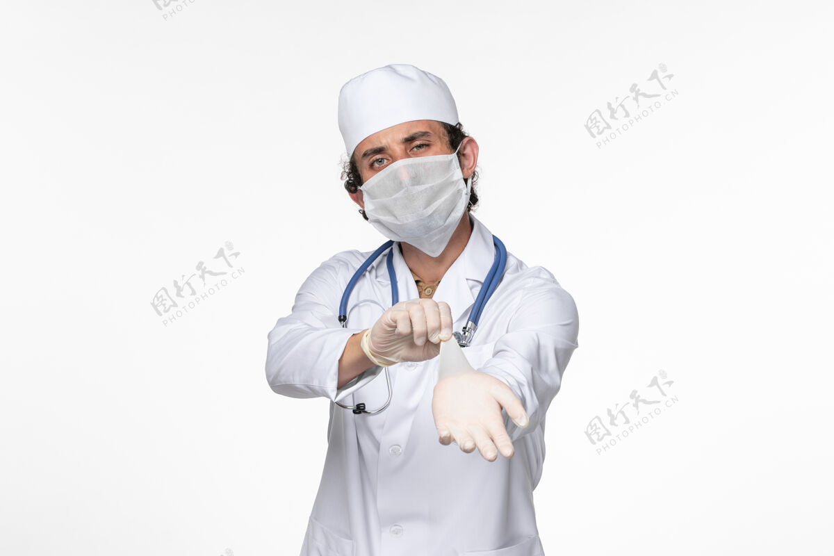 视图正面图男医生穿着医疗服 戴着无菌口罩作为防护罩 戴着白墙病毒手套就得了冠状病毒大流行病佩戴听诊器男性