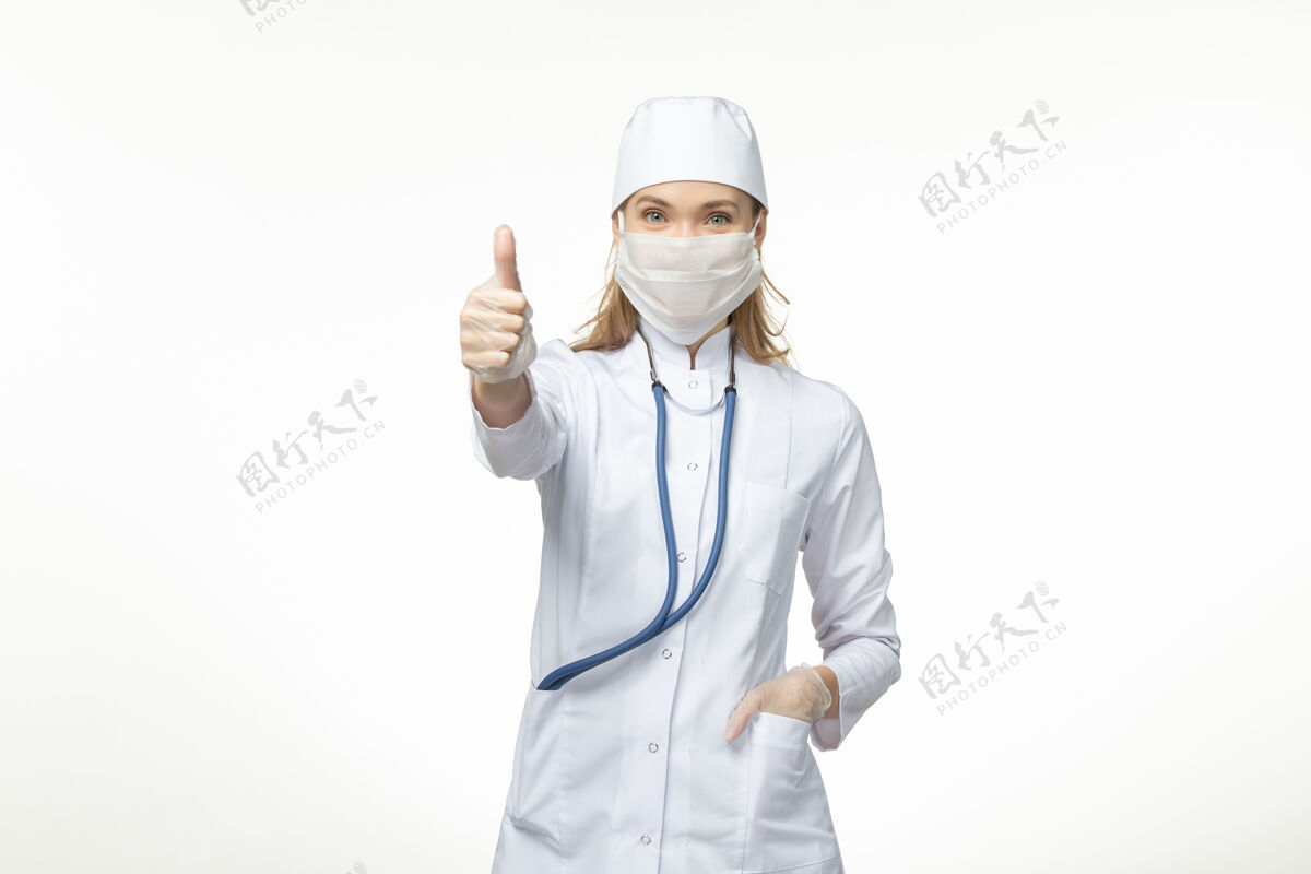 疾病正面图：身穿白色医疗服 戴着防冠状病毒面罩的女医生 微笑着面对白墙疾病——冠状病毒大流行套装疾病冠状病毒防护
