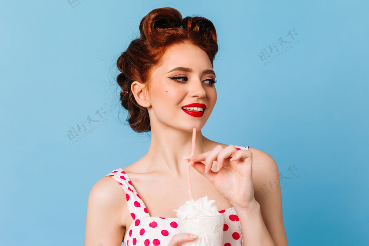 年轻人时尚的姜味女人在蓝色空间享受奶昔微笑的白人女孩在喝饮料波尔卡多时尚享受