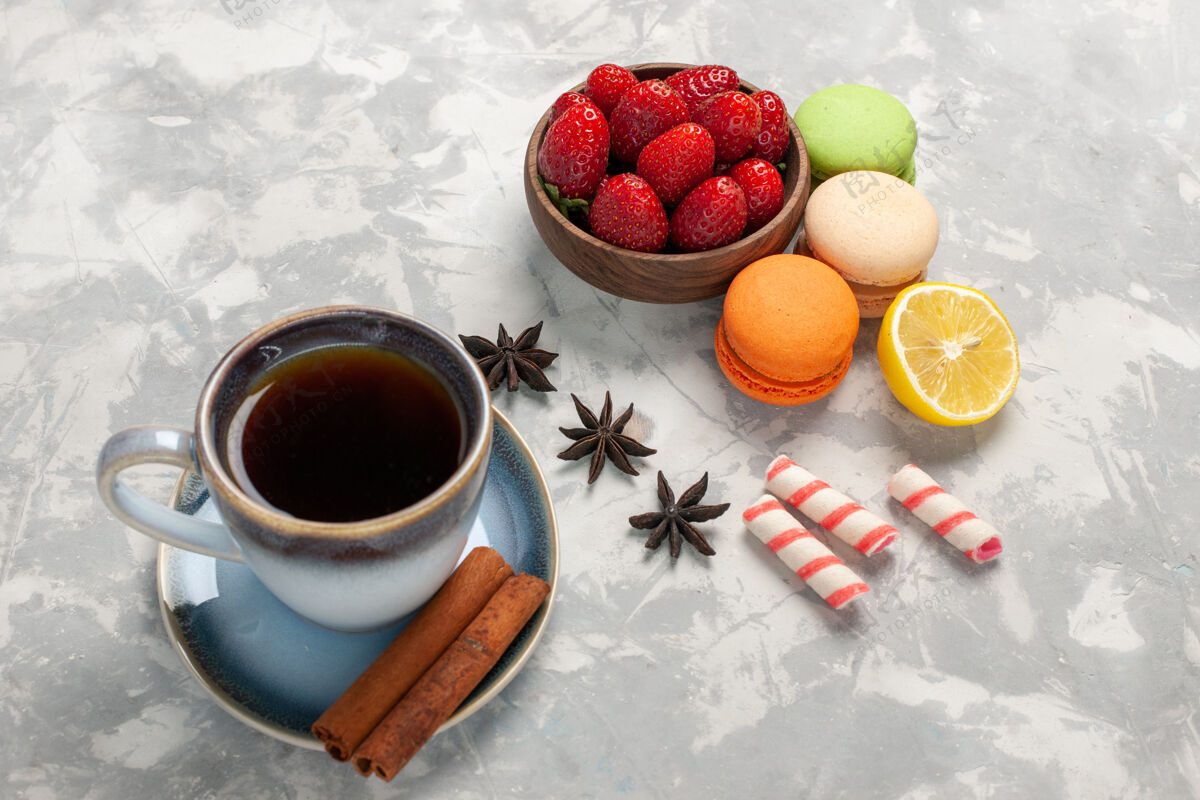 新鲜的正面图法国马卡龙 茶肉桂和新鲜草莓 白色表面 水果浆果蛋糕 饼干 甜甜的茶马克杯生的