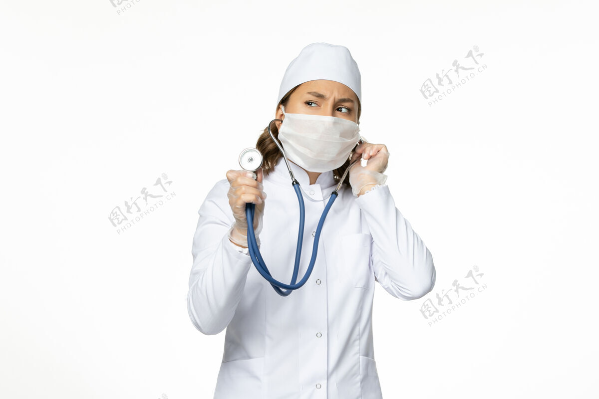 护士正面图女医生穿着白色的医疗服 戴着口罩 用听诊器在浅白的墙上贴着潘多米病毒病的药视图专业正面