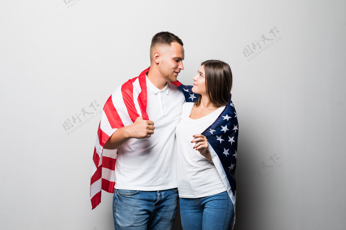 青少年一对漂亮的夫妇手里拿着美国国旗 遮住自己 看着彼此孤立在白色的天空开放享受欢呼
