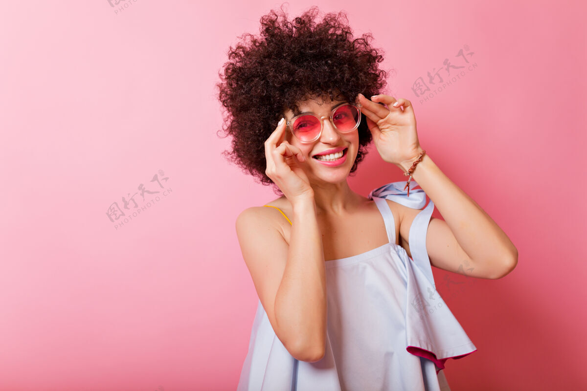 年轻阳光可爱的女人的肖像 短卷发 迷人的微笑 穿着蓝色衬衫 戴着粉色眼镜 在粉红色的脸上摆姿势女人时髦黄色