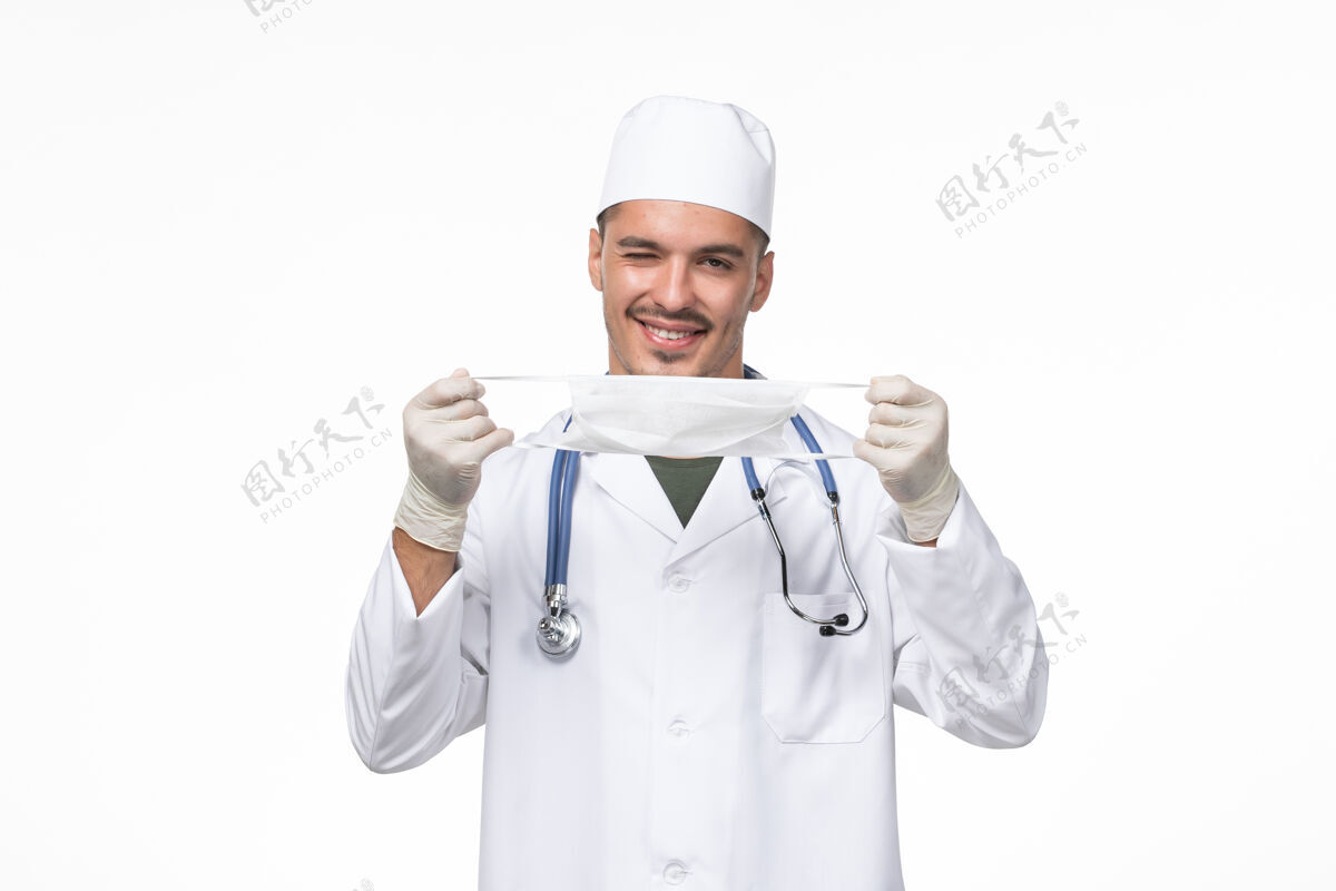 桌子正面图：男医生身着医疗服 戴着防冠状病毒口罩 白色办公桌上病毒冠状病毒-疾病大流行正面疾病人