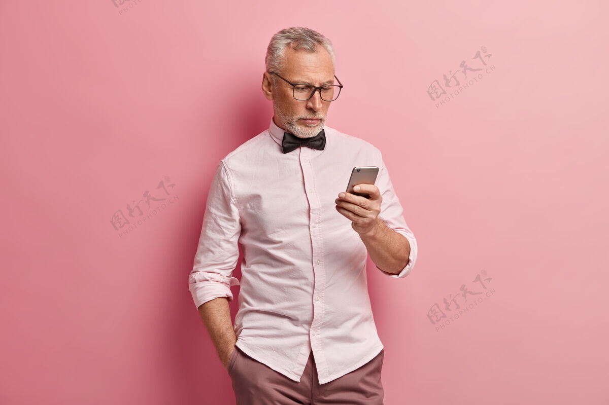 老严肃的成熟男人使用智能手机 在线阅读新闻 把手放在口袋里 总是保持联系 在粉色背景下与世隔绝男士一个老年人