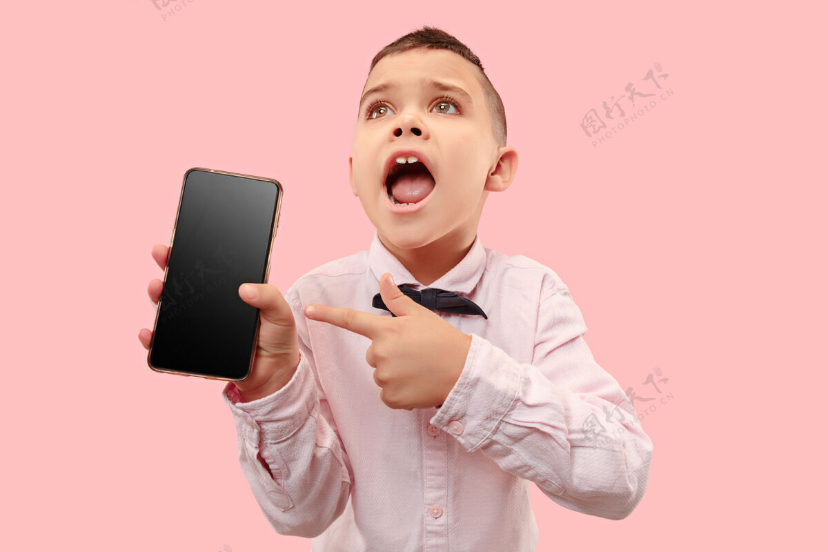 显示室内肖像的迷人的年轻男孩拿着空白的智能手机技术手机电话