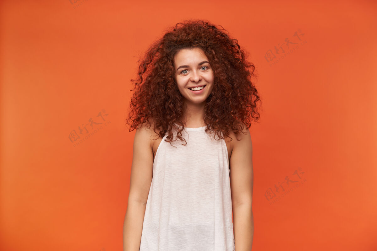 年轻有魅力的成年红发女孩的肖像 卷发穿着白色露肩上衣头发凌乱 面带微笑隔着橙色的墙20多岁皮肤凌乱